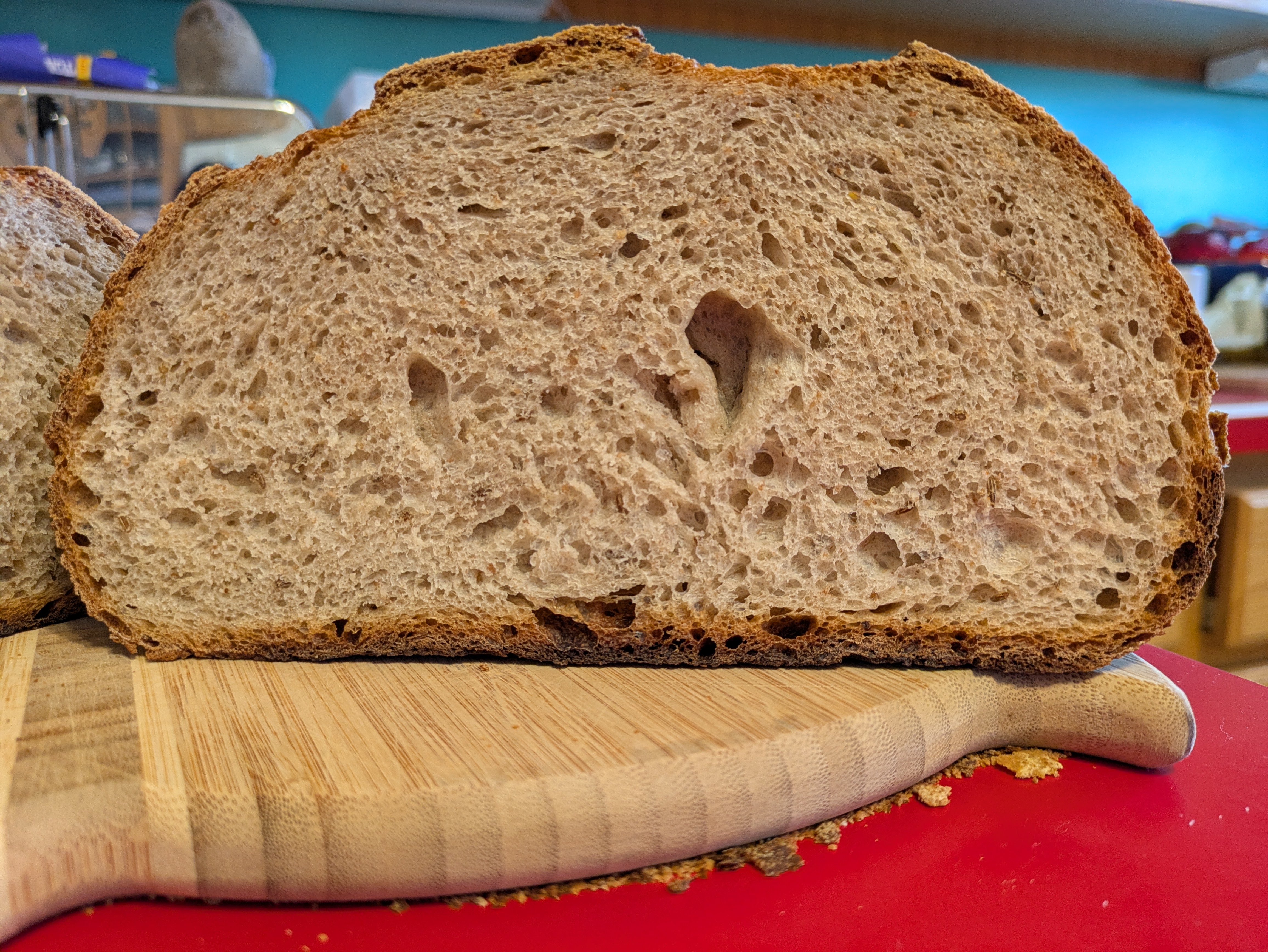 Crumb shot of a large loaf of bread on a wooden cutting board. The golden crust is very defined against the light, airy interior of the bread.