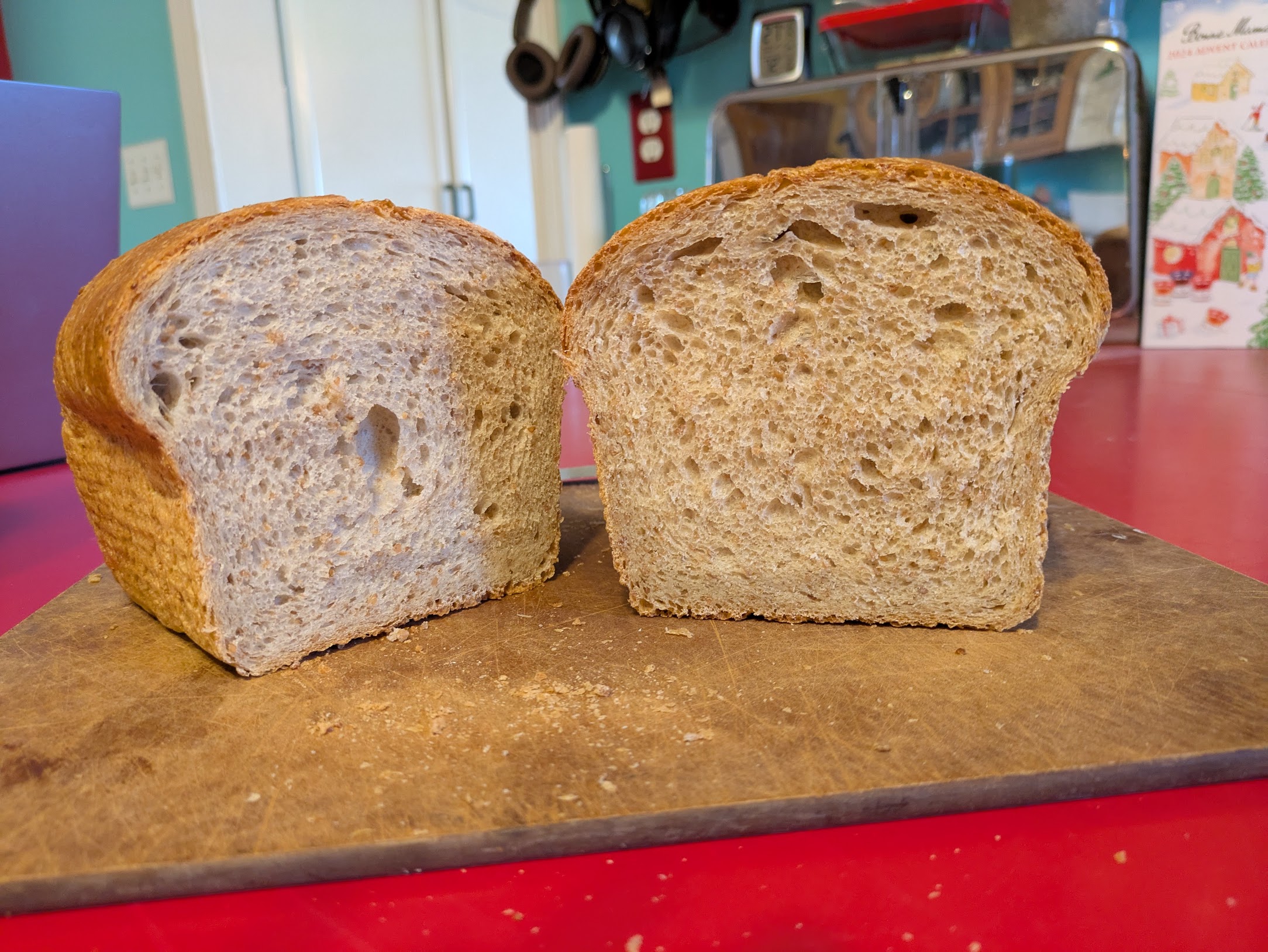 A sandwich loaf of bread, cut in half, on a cutting board. The photo shows the interior crumb on both halves. It is light beige to tan with plenty of air and a soft look. The crust is blonde/tan and very defined.