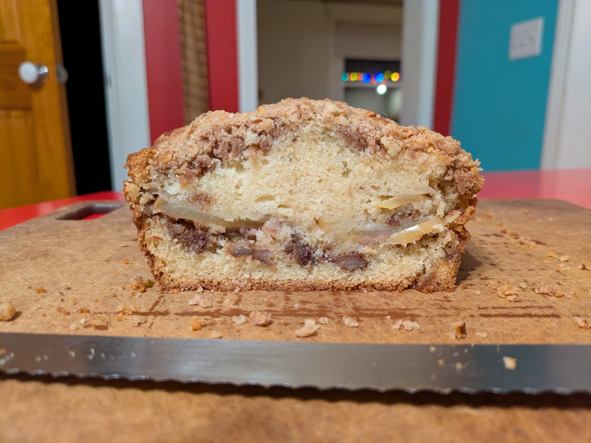 A photograph of the bread interior, in profile (crumb shot). The interior almost slightly yellow-tinged and there is a seam of apple slices and crumb running across the center of the bread. The crust and top crumble are very defined against the interior.