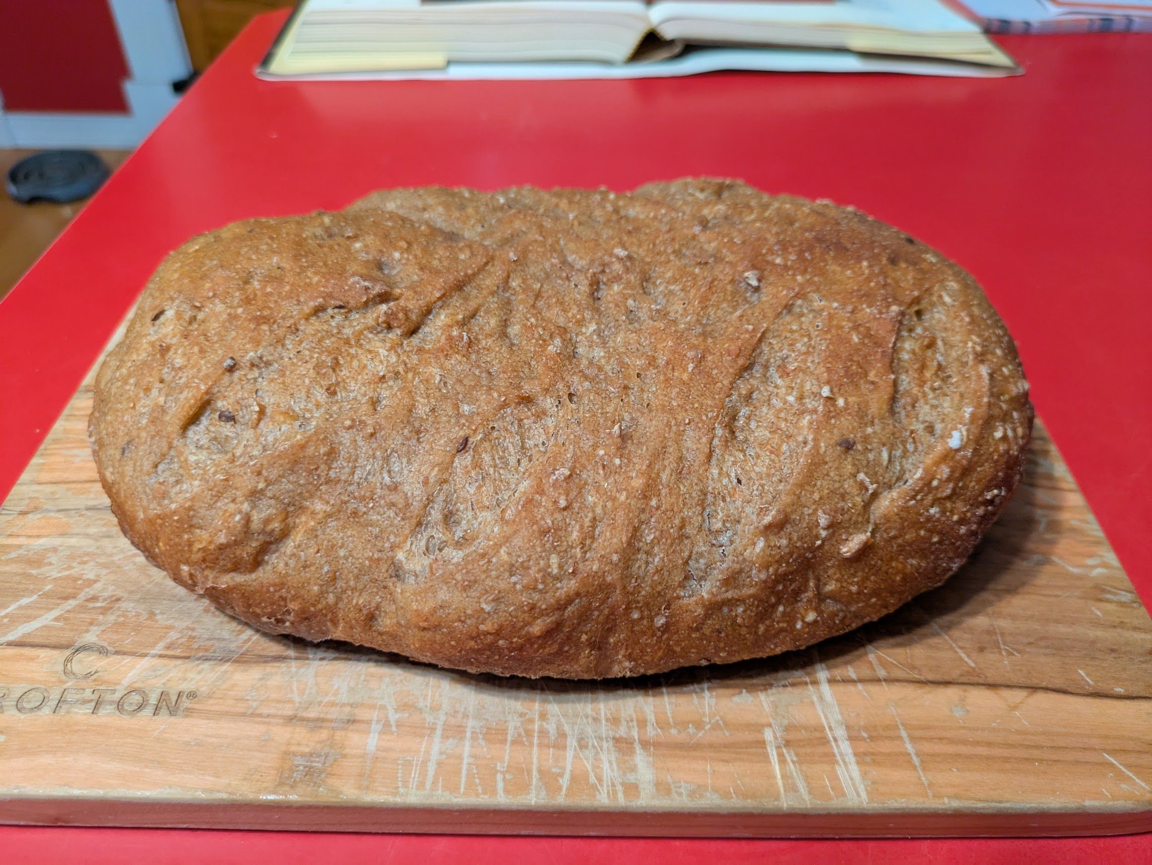 An oval-ish loaf of bread on a cutting board. The bread is golden brown and a few score lines are barely visible.