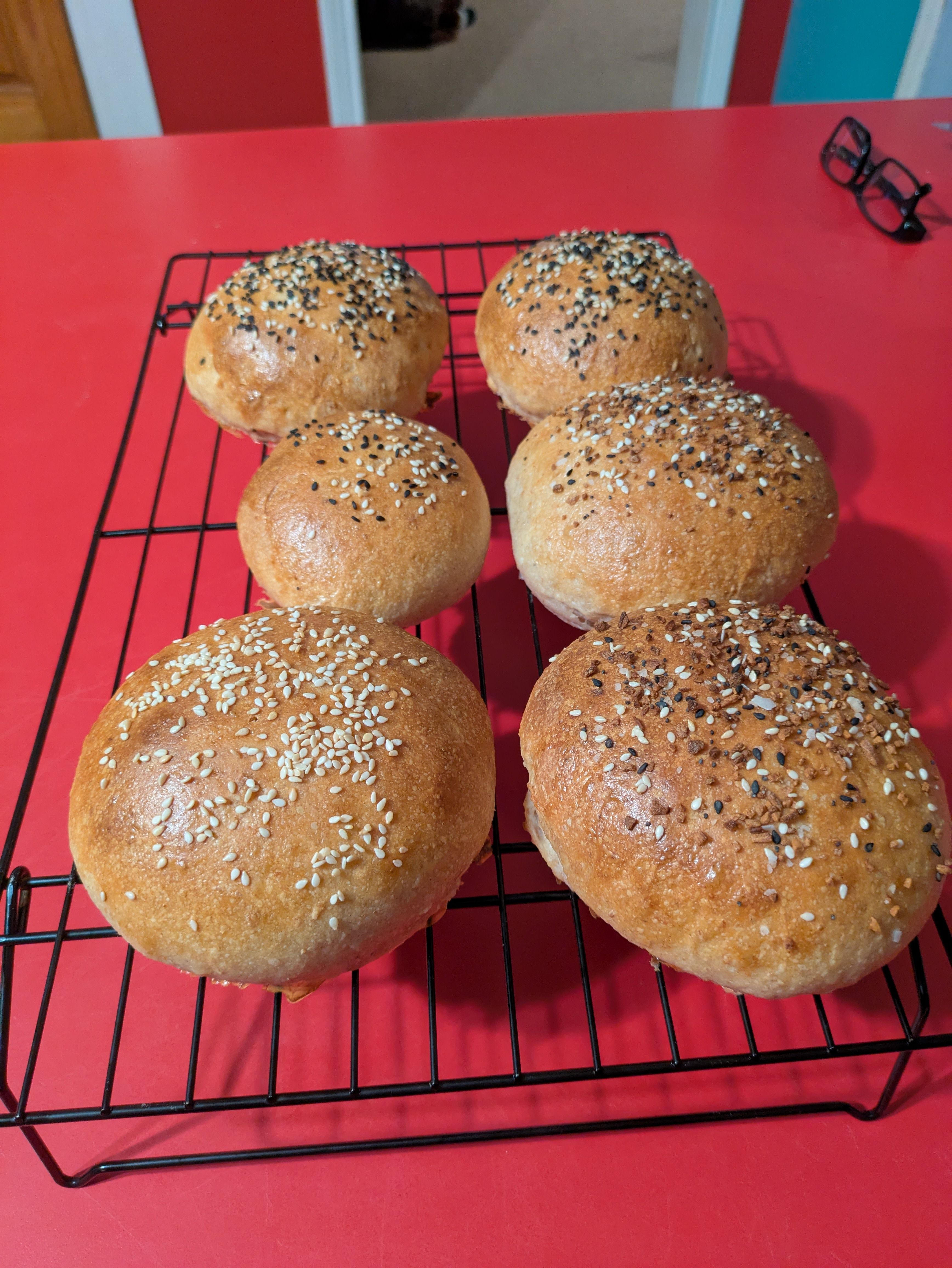 6 Golden brown buns topped with seeds, on a black wire cooling rack.