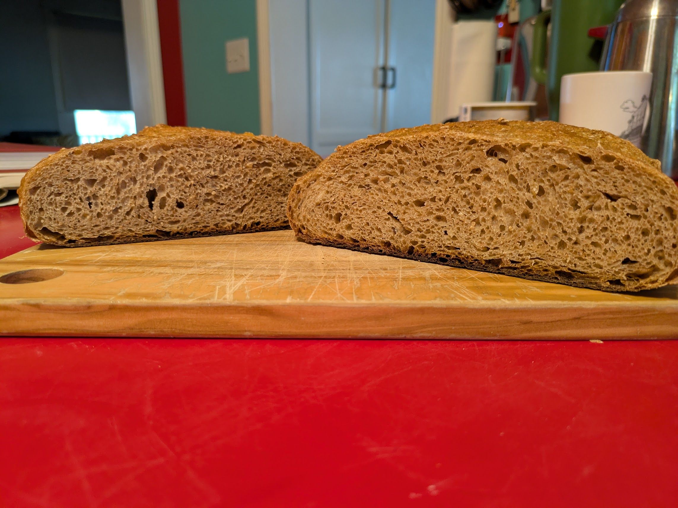 Two halves of a loaf of bread, cut-side facing the camera, resting on a cutting board. The light tan crumb of the bread is fairly open with a golden crust.