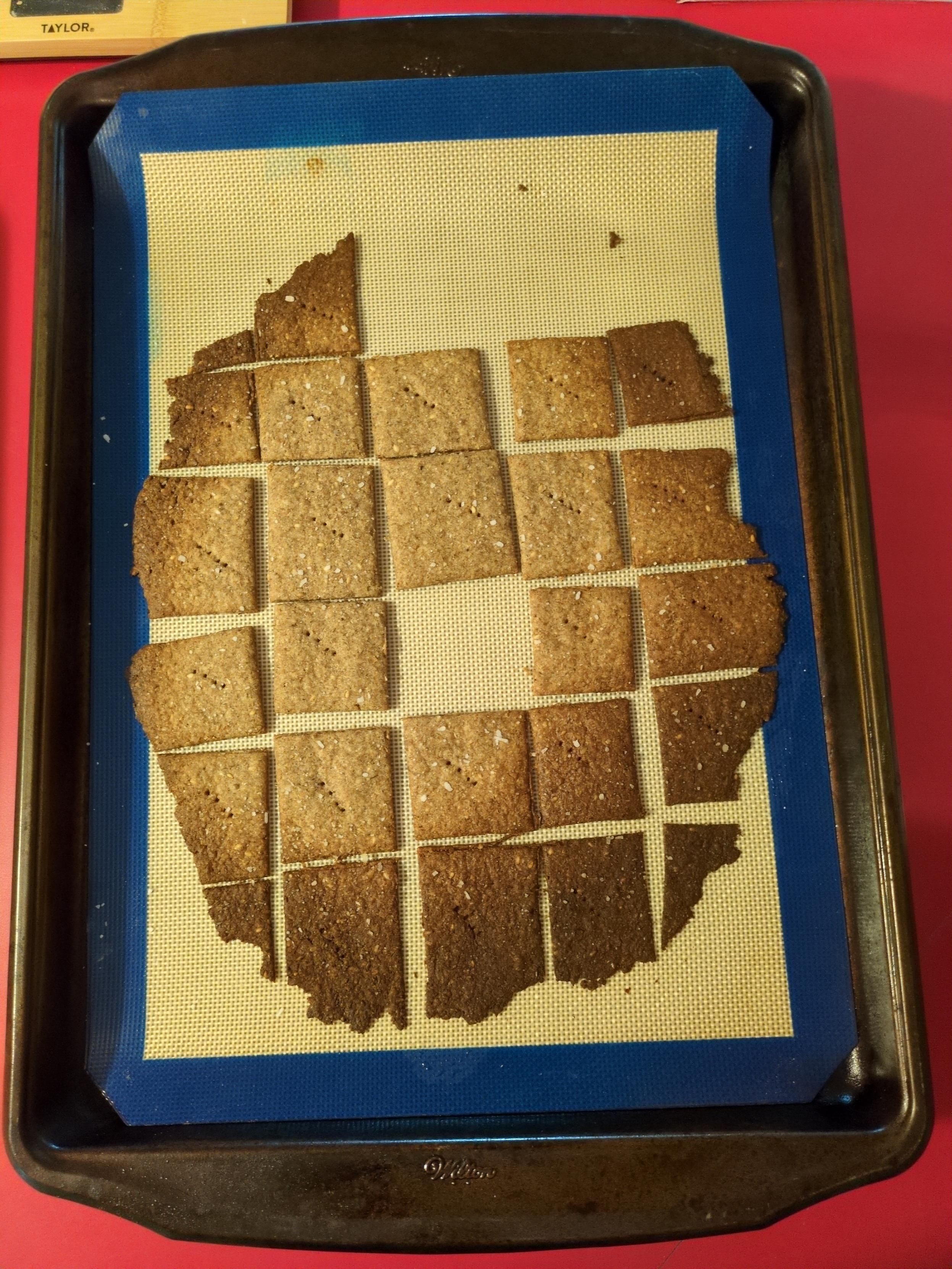 Photo of a baking sheet of crackers, some missing from what would have formed an oval. The crackers range from tan in the center to dark brown on the edges.